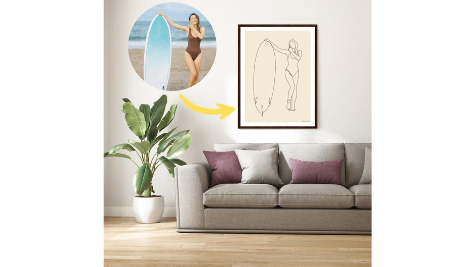 Custom printed line art of a surfer holding her surfboard on the beach. The printed poster is on the wall of the living room, over a sofa and a plant. There is a photo to show the before and after result.
