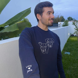 Smiling man wearing his custom embroidered sweatshirt with line art of his two dogs. Sleeve text with the name of his dogs and a heart is visible.