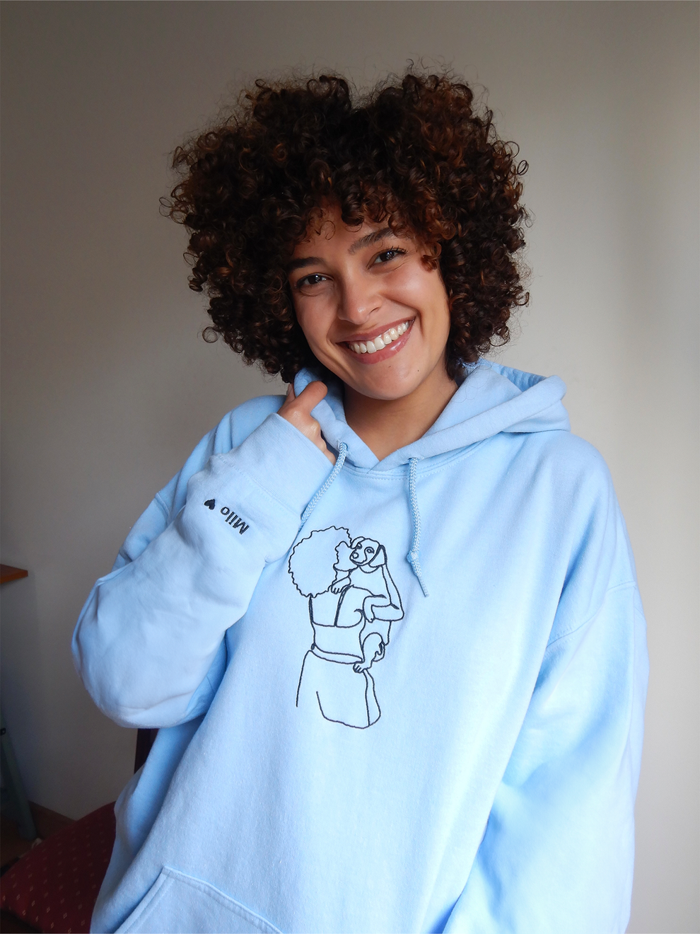 BLM woman wearing her custom embroidered blue hoodie with a portrait of her holding her dog in the arms.